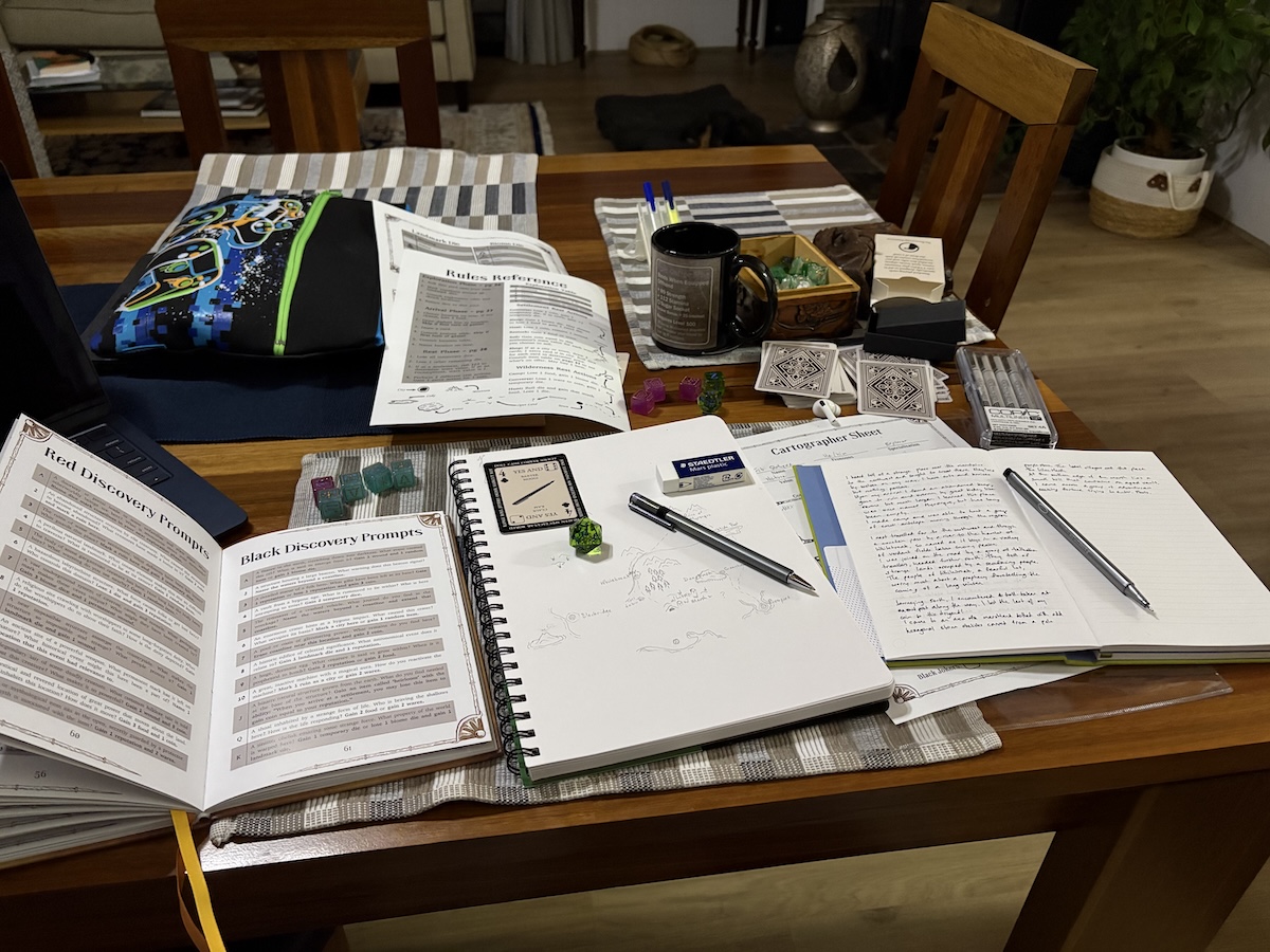 A table covered with materials used in a roleplaying game. Visible are rules, notebooks and paper, pens and pencils, dice, and playing cards.